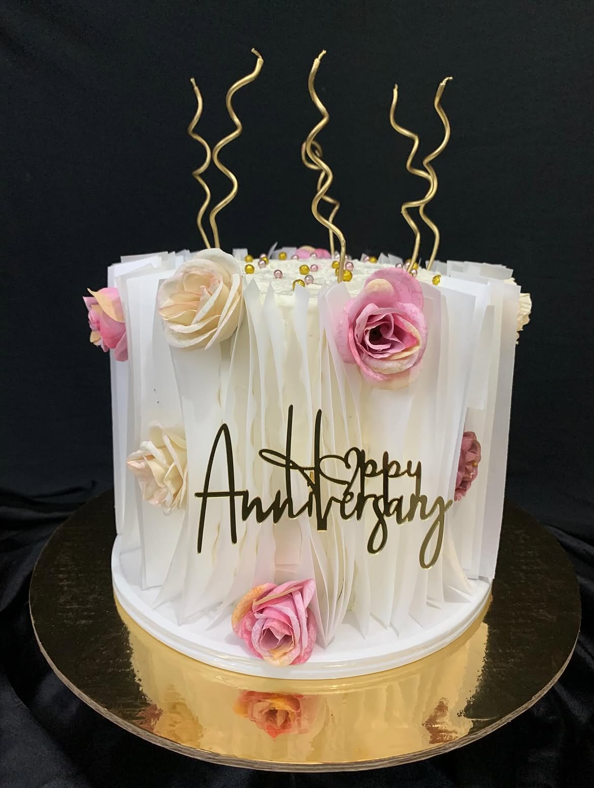 Pastel blanco de aniversario con rosas y velas doradas